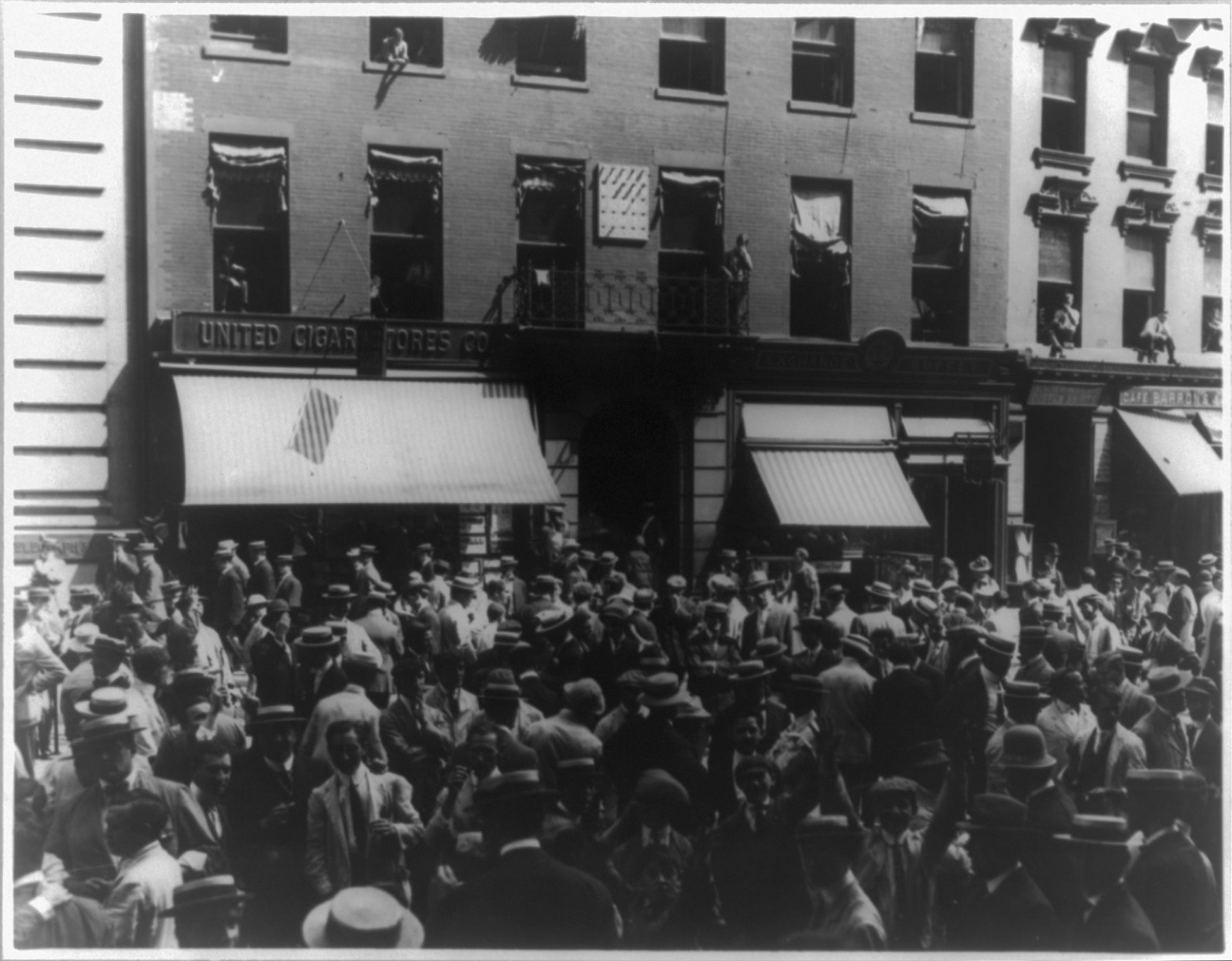 A crowd of brokers in the street below office windows, with clerks leaning out of the windows