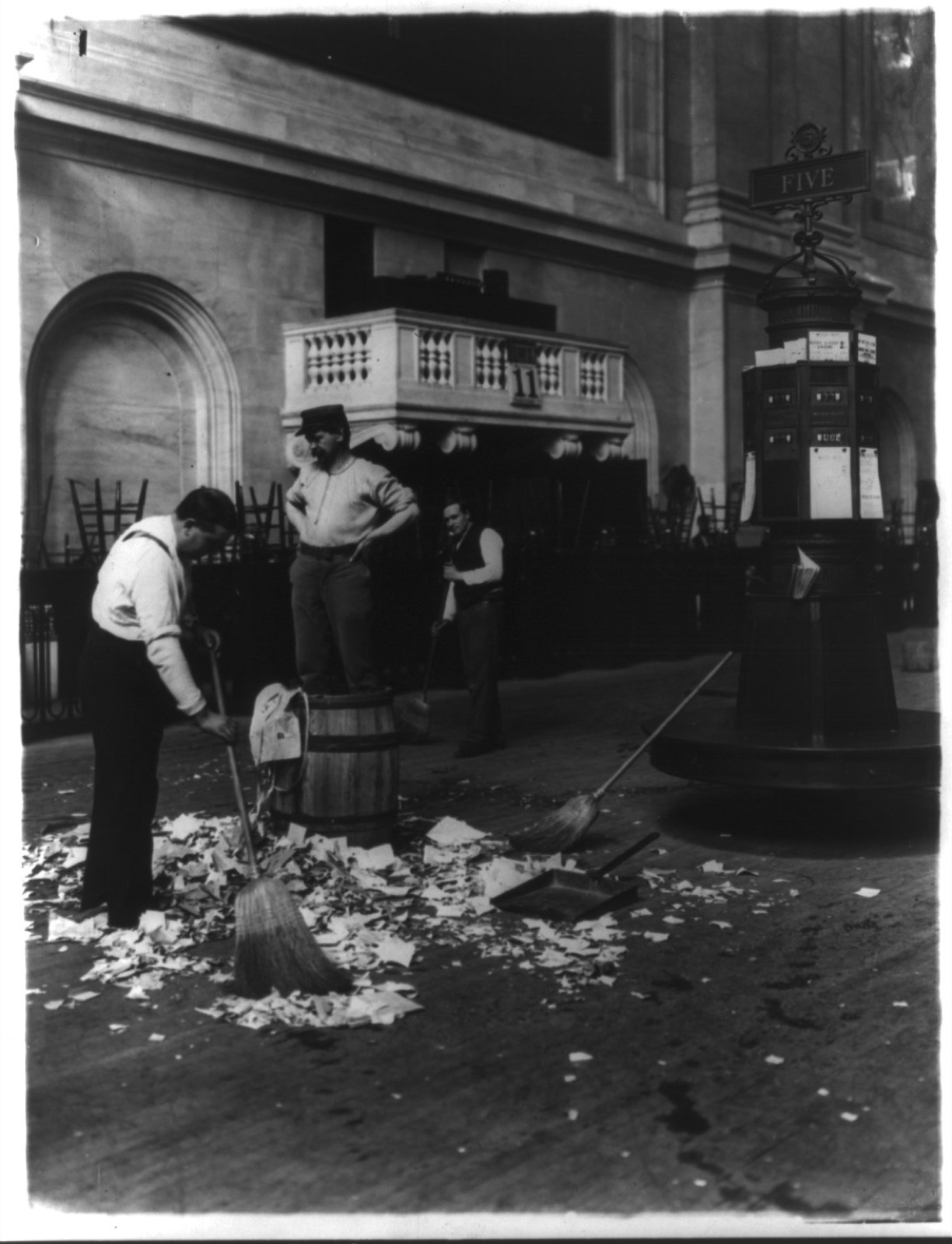 Men sweeping heaps of paper slips from the floor of the stock exchange